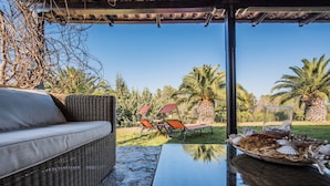 Un área de estar al aire libre techada con mobiliario de mimbre, una mesa de vidrio y una decoración central.