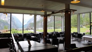 Un restaurante con amplios ventanales que ofrecen vistas a la montaña, pilares de madera e iluminación colgante moderna.