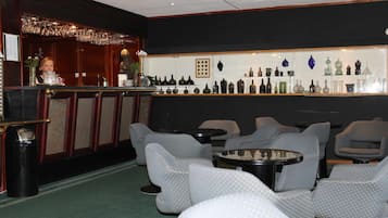 Zona de bar con una variedad de copas a la vista, asientos con tela estampada y una barra con un cantinero.