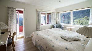 Un dormitorio con una cama grande, una silla, una mesita y vistas al exterior a través de una ventana.