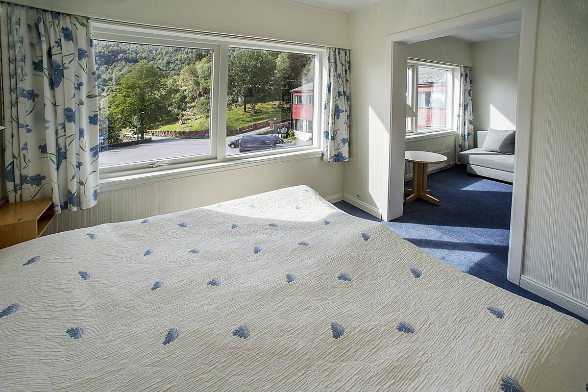A bedroom with a large bed, a small table, a sofa, and a window with curtains.