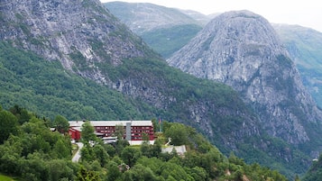 A hotel with a modern design, situated in a mountainous area with lush greenery and rocky terrain.