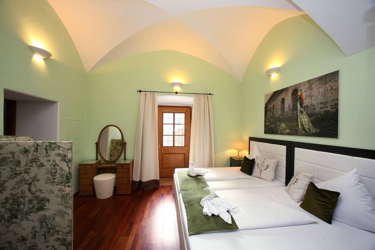 A hotel room with two beds, a wooden dresser, a mirror, a painting on the wall, and a window with curtains.