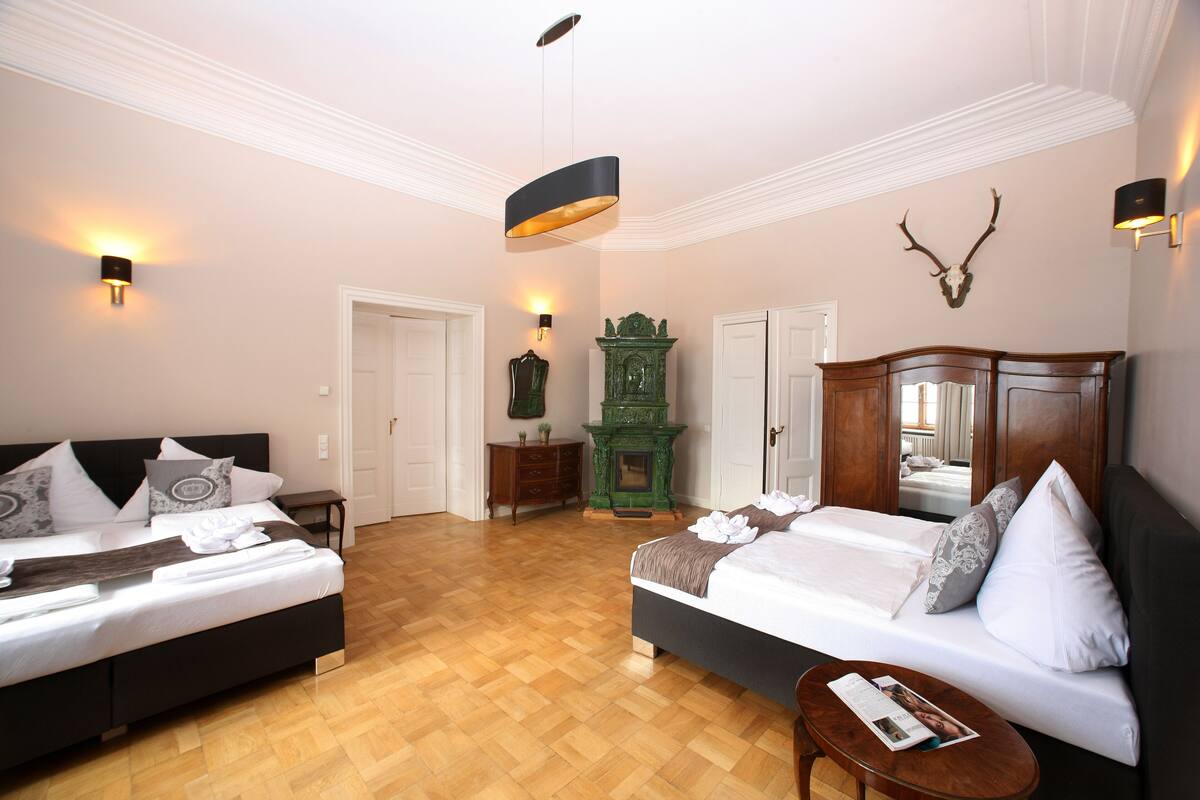 A hotel room with two beds, a wooden floor, a green fireplace, and a deer head on the wall.