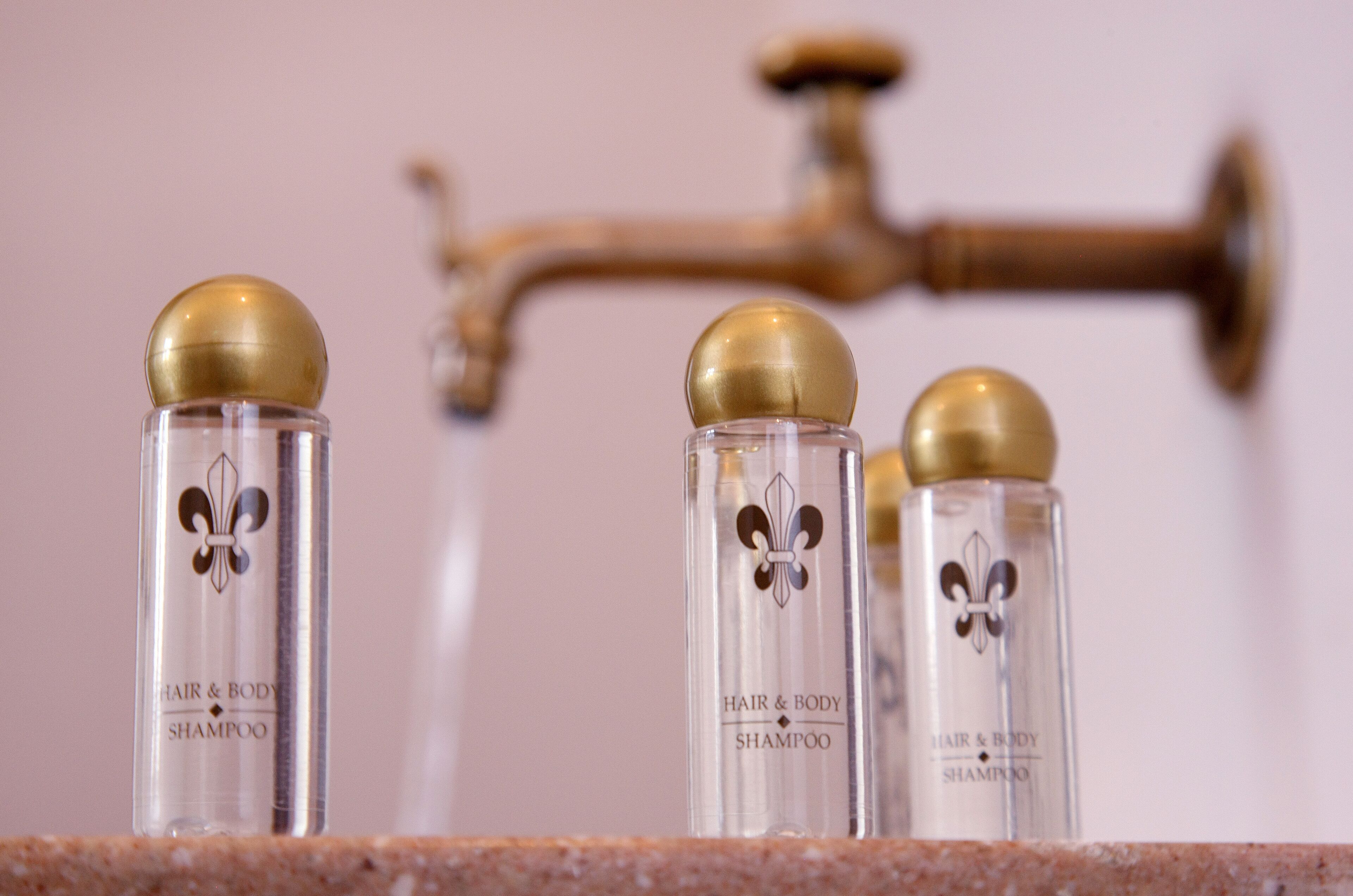 Three bottles of hair and body shampoo on a countertop with a brass faucet in the background.