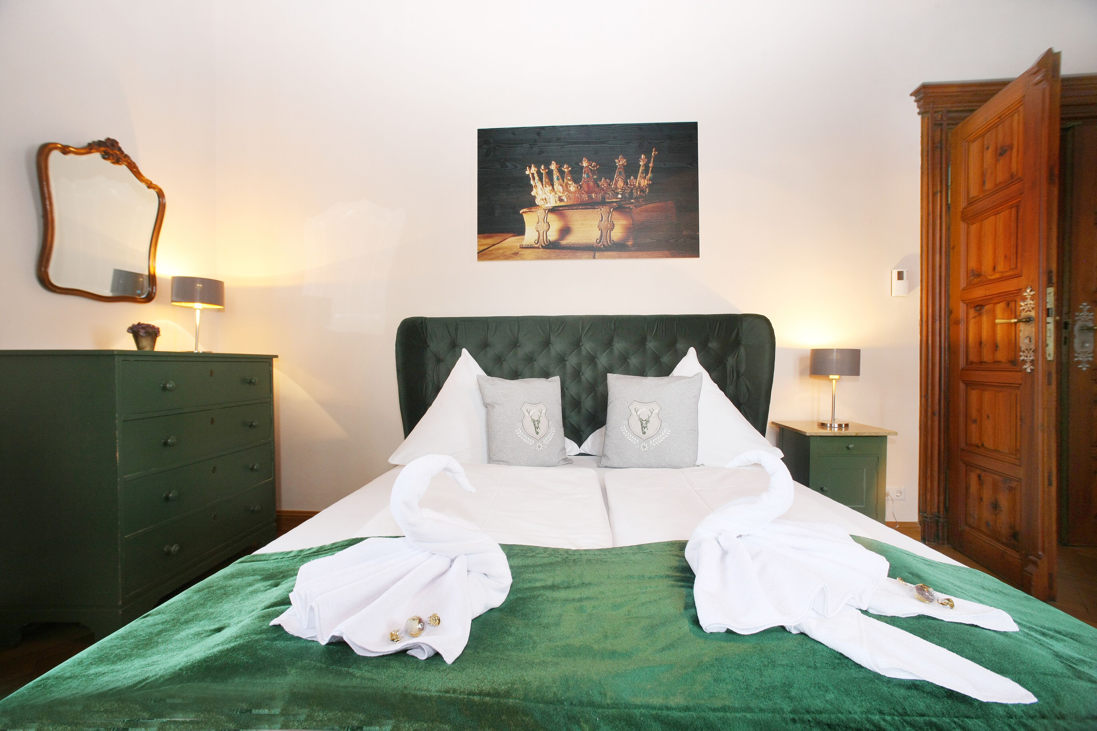A neatly made bed with a green bedspread, two pillows, and two white towels folded on the bed.