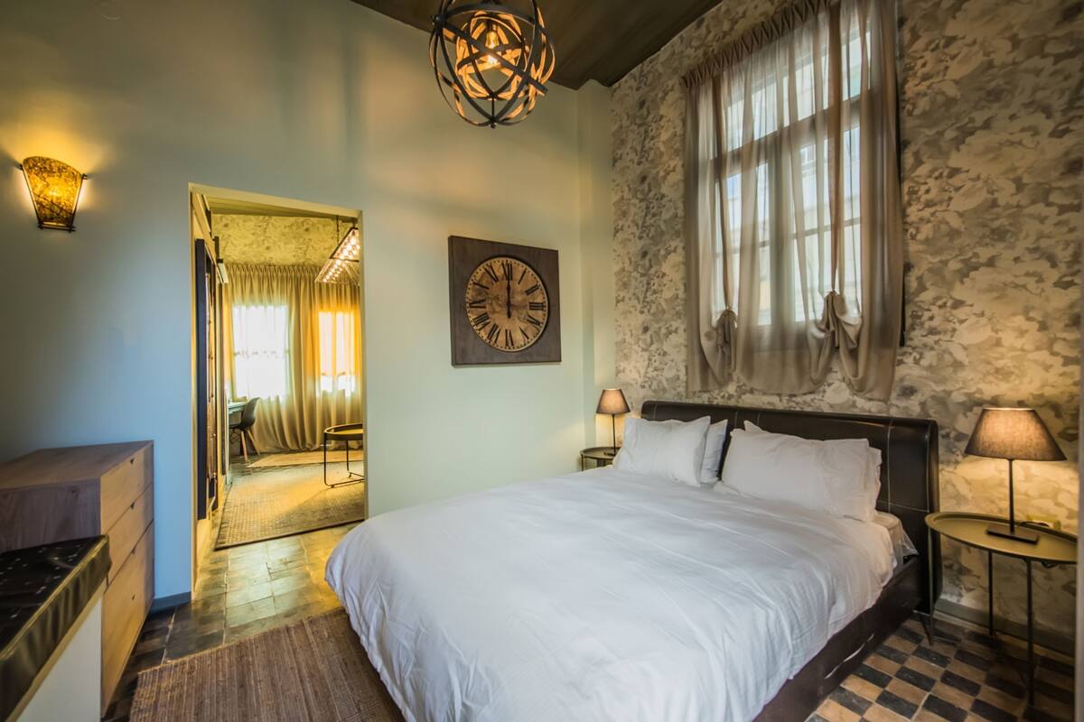 Une chambre à coucher avec un grand lit, une tête de lit en bois, une horloge murale et un mur en pierre.