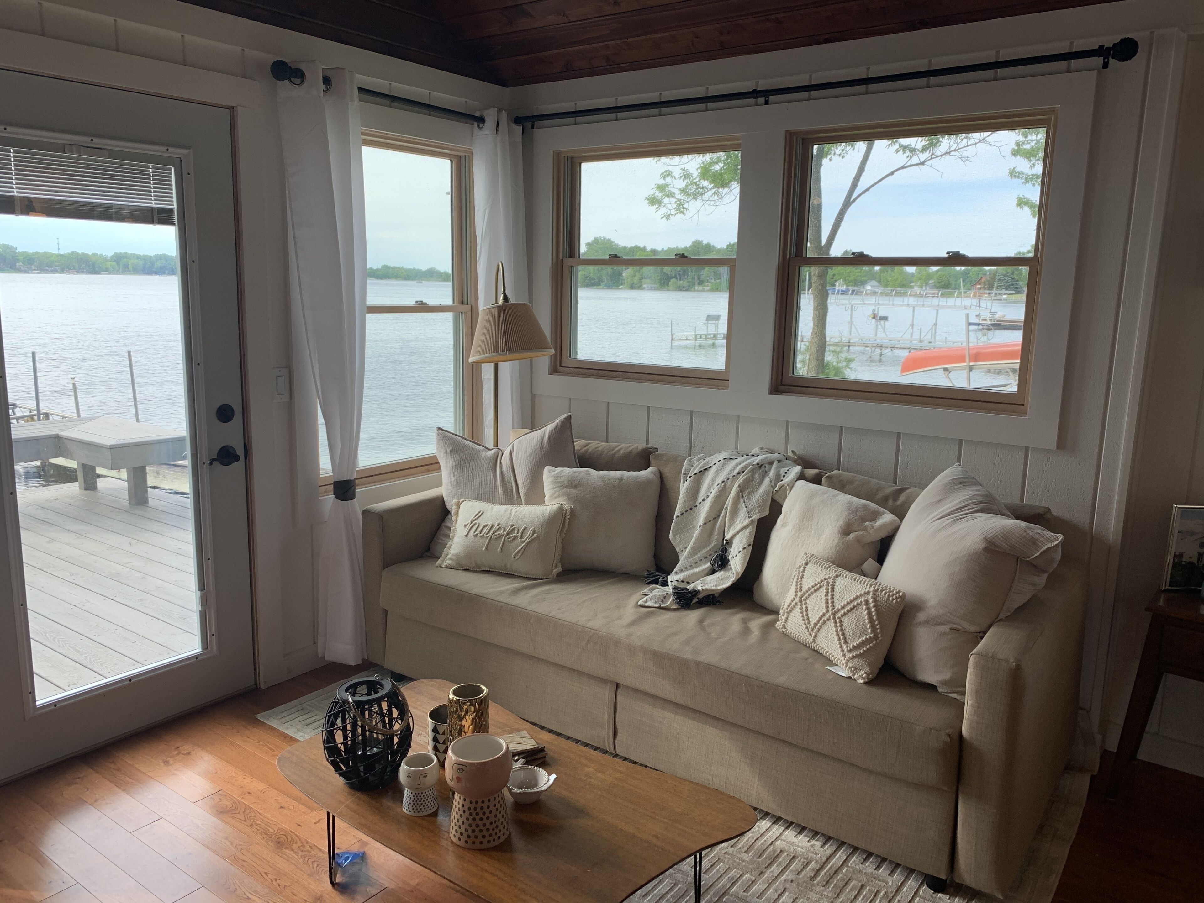 A cozy room with a beige sofa, a wooden coffee table, and a view of the water through large windows.