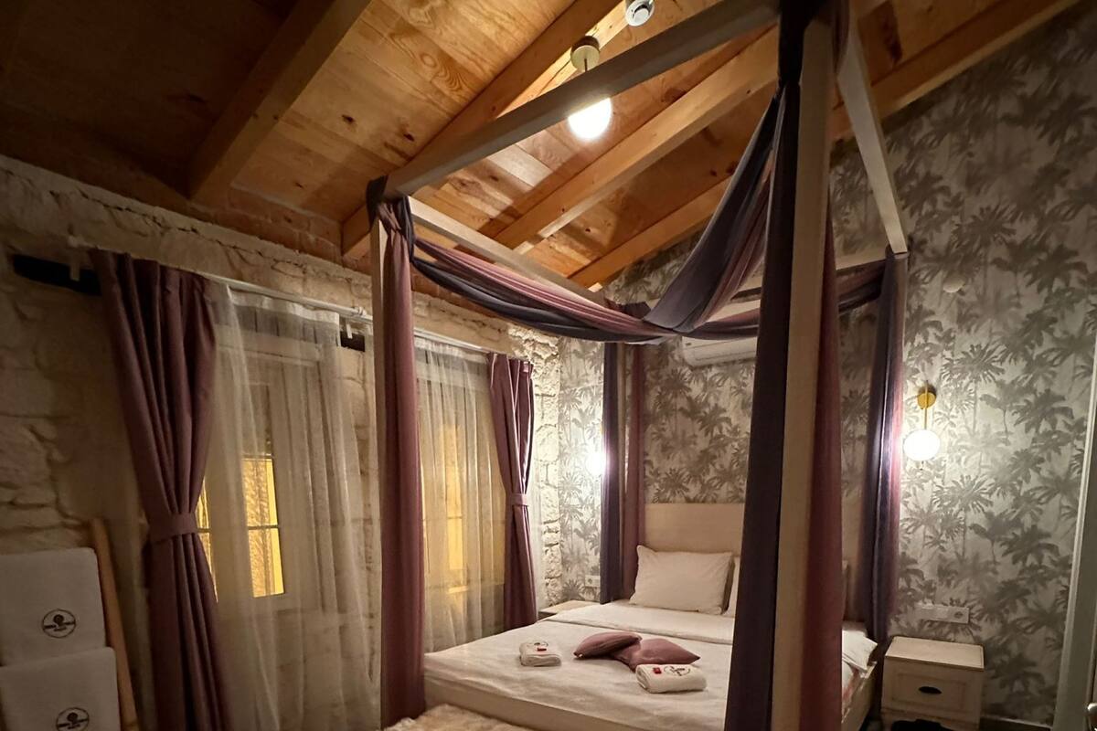 Una habitación con una cama con dosel, una pared de piedra, un techo de madera y una mesita de noche pequeña.