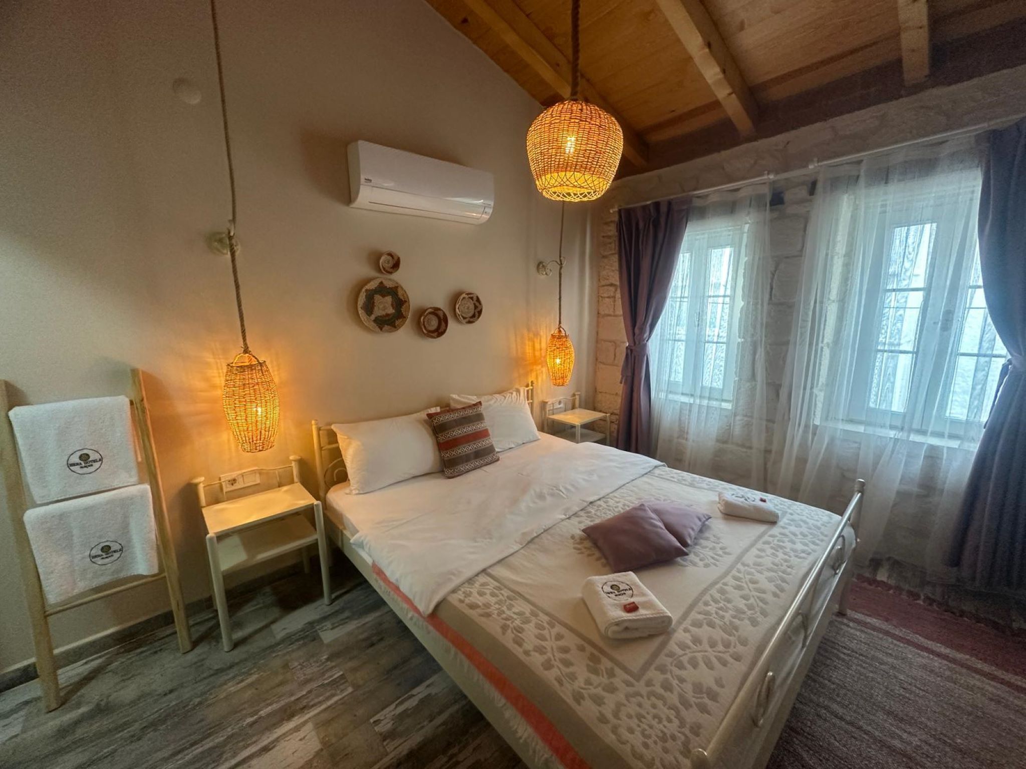 A bedroom with a bed, bedside tables, an air conditioner, decorative wall plates, and a window with curtains.