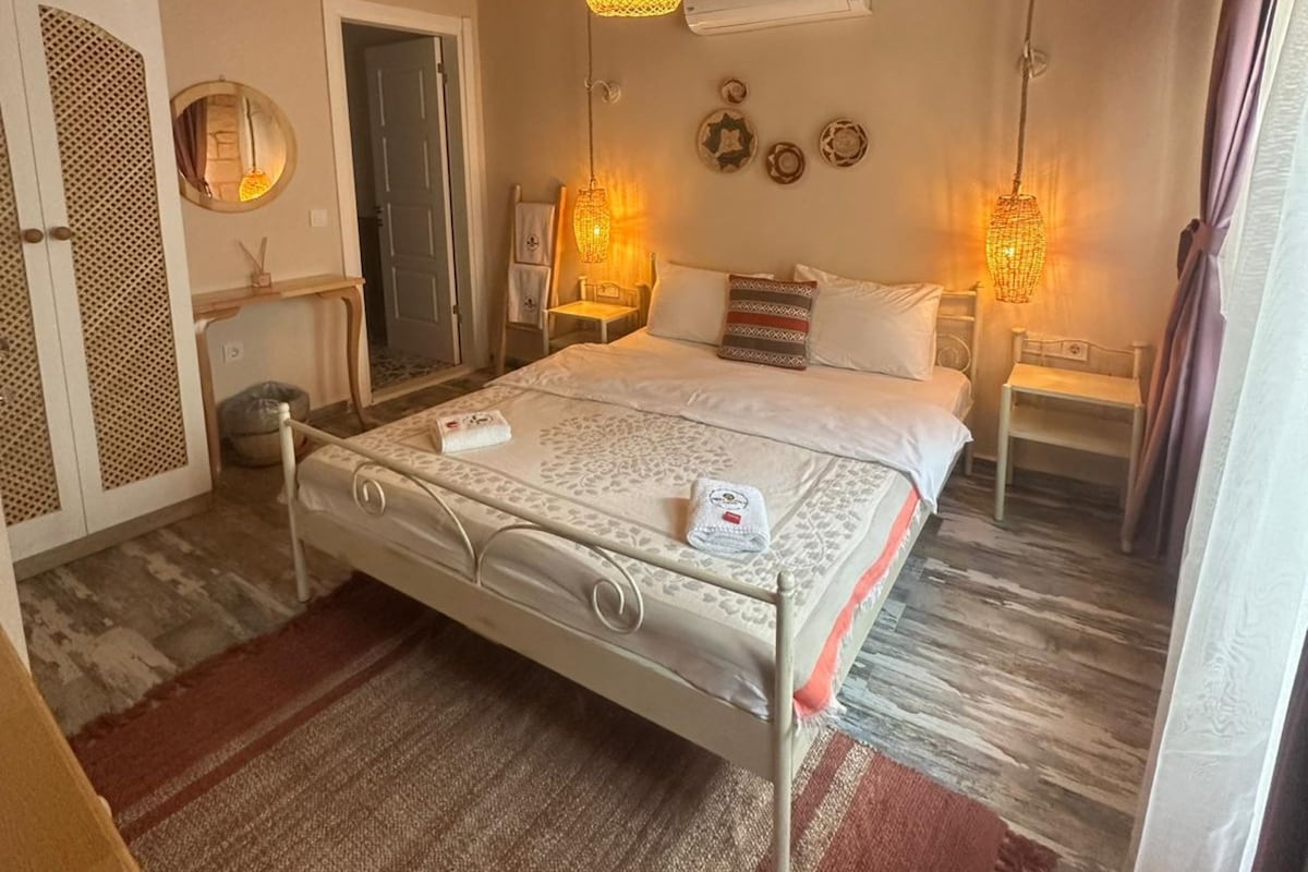 A bedroom with a bed, two bedside tables, an air conditioning unit, and a wooden ceiling.