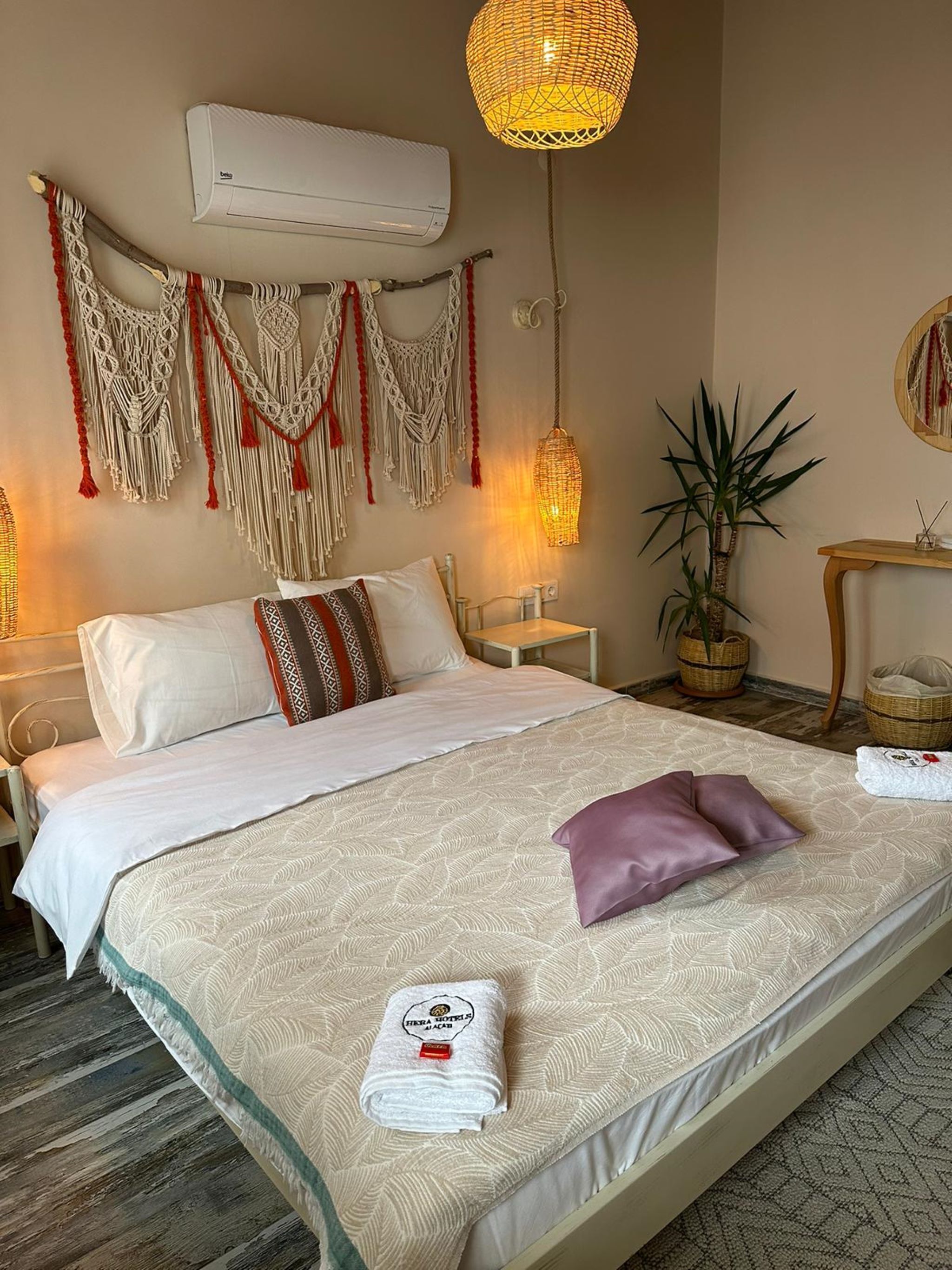 A neatly made bed with a patterned bedspread, a decorative macrame wall hanging, a hanging lamp, and a potted plant.