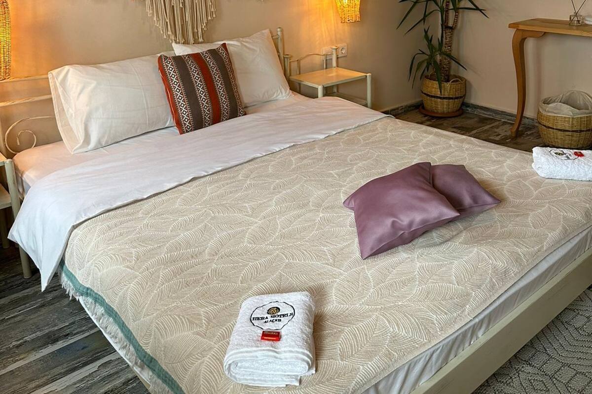 Una cama bien hecha con una colcha estampada, un tapiz decorativo de macramé, una lámpara colgante y una planta en maceta.