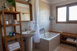 A bathroom with a bathtub, a sink, a mirror, and shelves with toiletries.