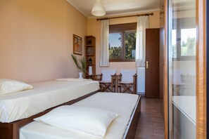 A room with two beds, a wooden chair, a small table, and a window with curtains.
