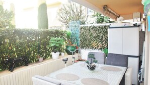 En terrasse med et bord, stole, plantekasser og et køleskab.