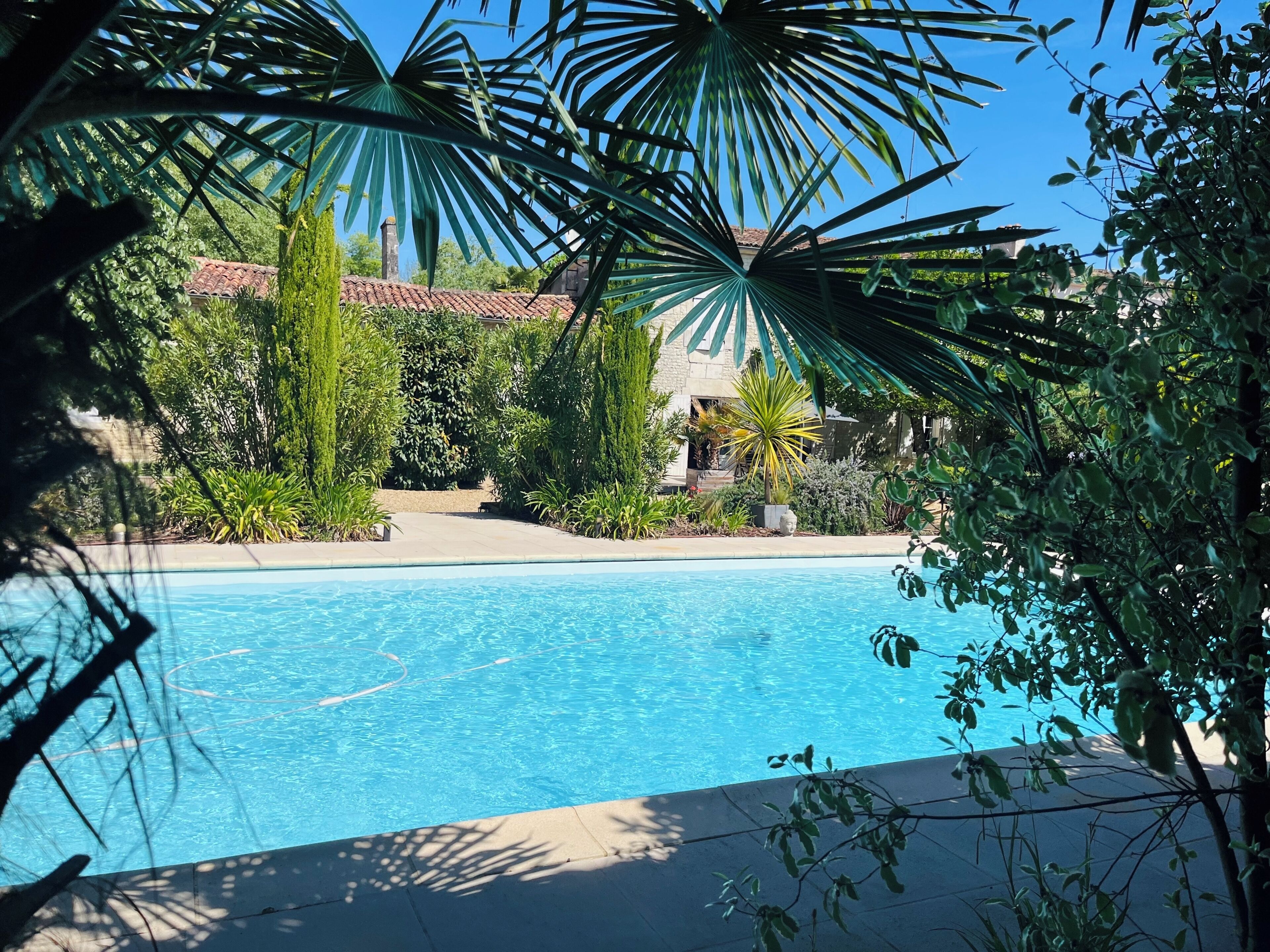 A clear blue pool surrounded by lush greenery and a stone building with a tiled roof.