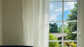 Ein Zimmer mit einem dunkelblauen Sofa, einer weißen Tür und Blick auf Grünflächen sowie ein Gebäude.