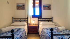 A room with two beds, a nightstand with a lamp, and a window with curtains.