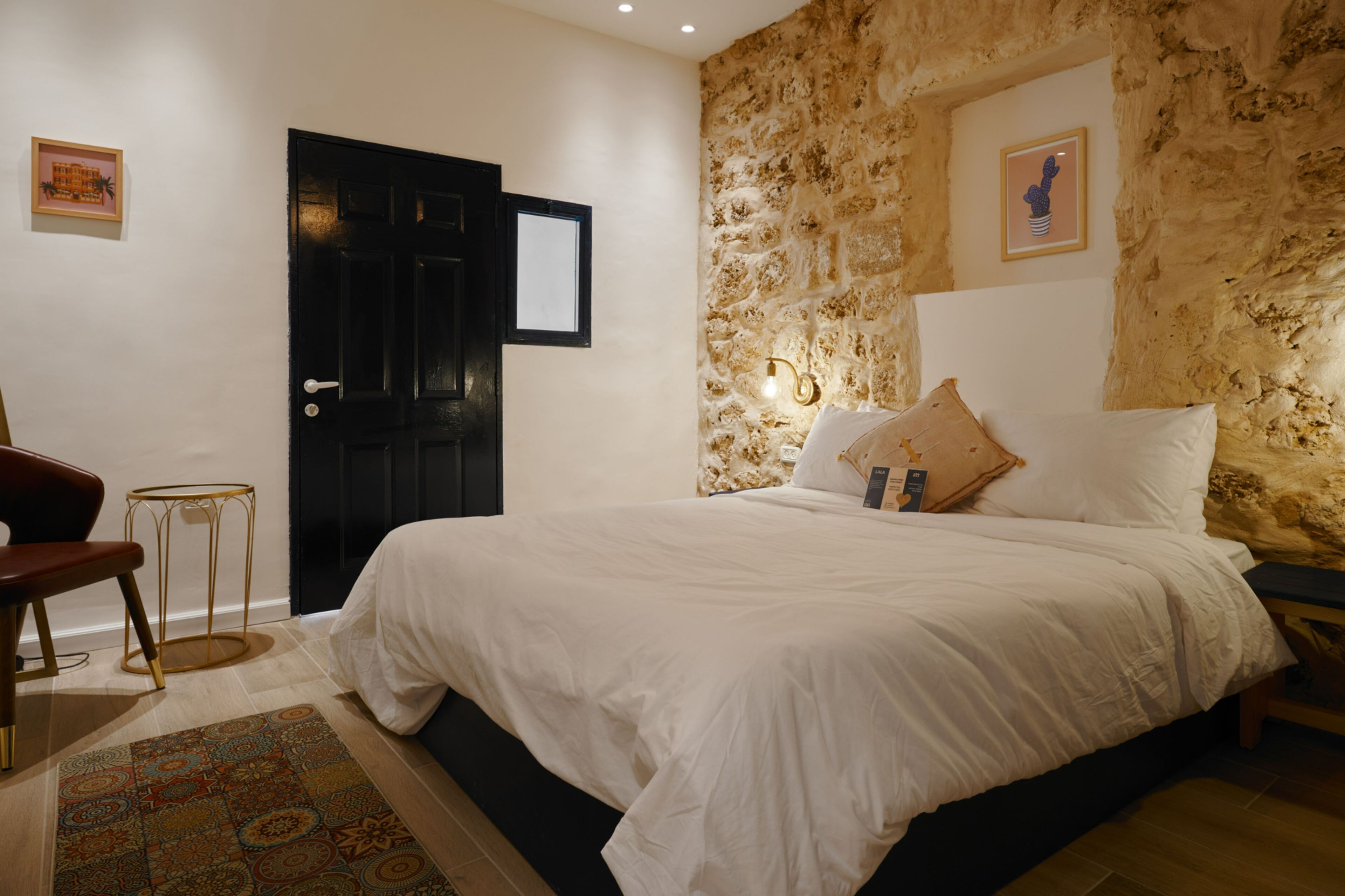Ein Schlafzimmer mit Steinwand, einem Bett mit weißer Bettwäsche, einer schwarzen Tür und einem kleinen runden Tisch mit Stuhl.