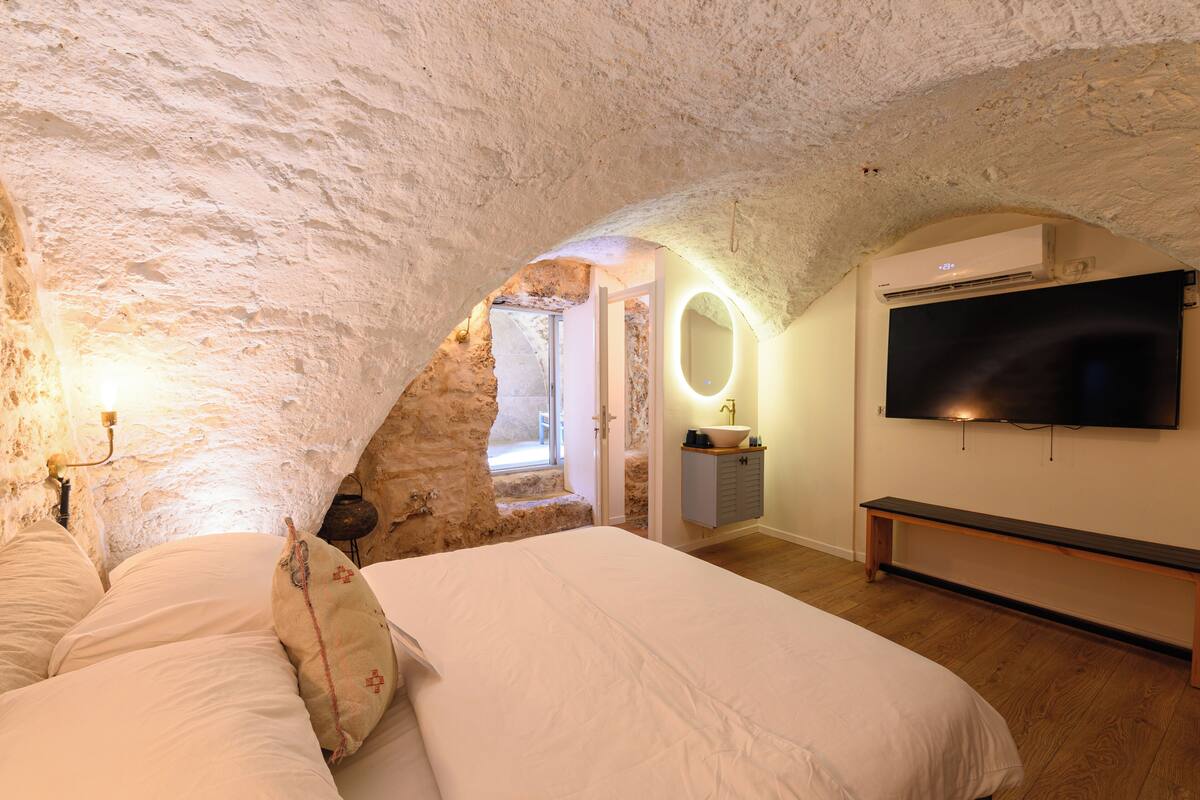A bedroom with a stone ceiling, a bed, a TV, and a small bathroom.