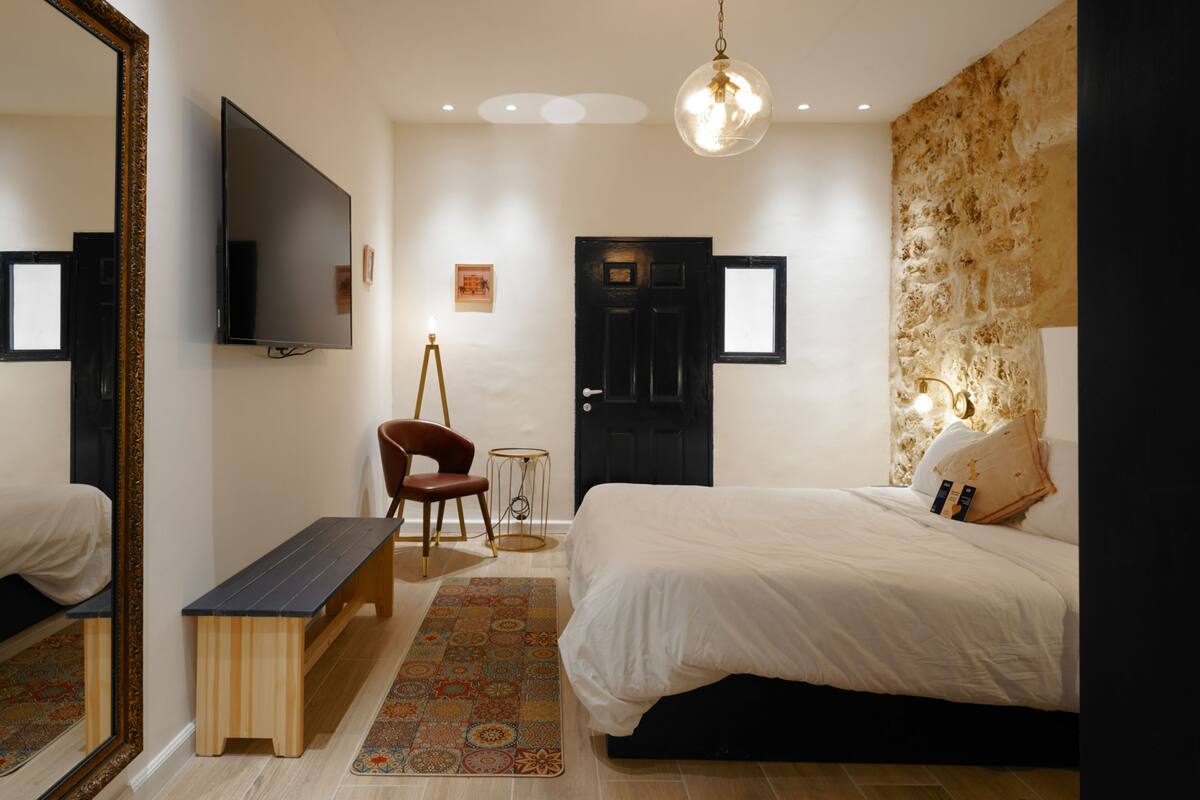 A bedroom with a bed, a bench, a chair, a television, and a door.