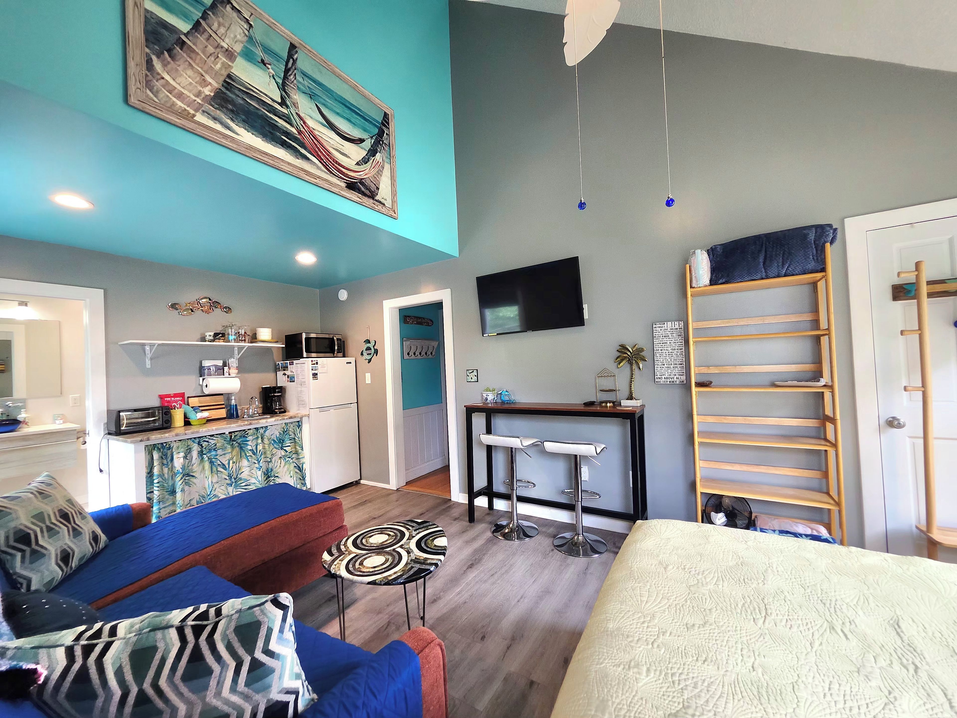 A compact living space with a kitchenette, a sofa, a bed, and a TV mounted on the wall.