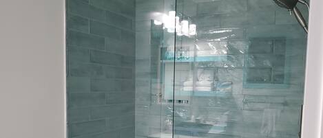Une salle de bain avec une douche à parois de verre, des toilettes et une étagère en verre où sont rangés les articles de toilette.
