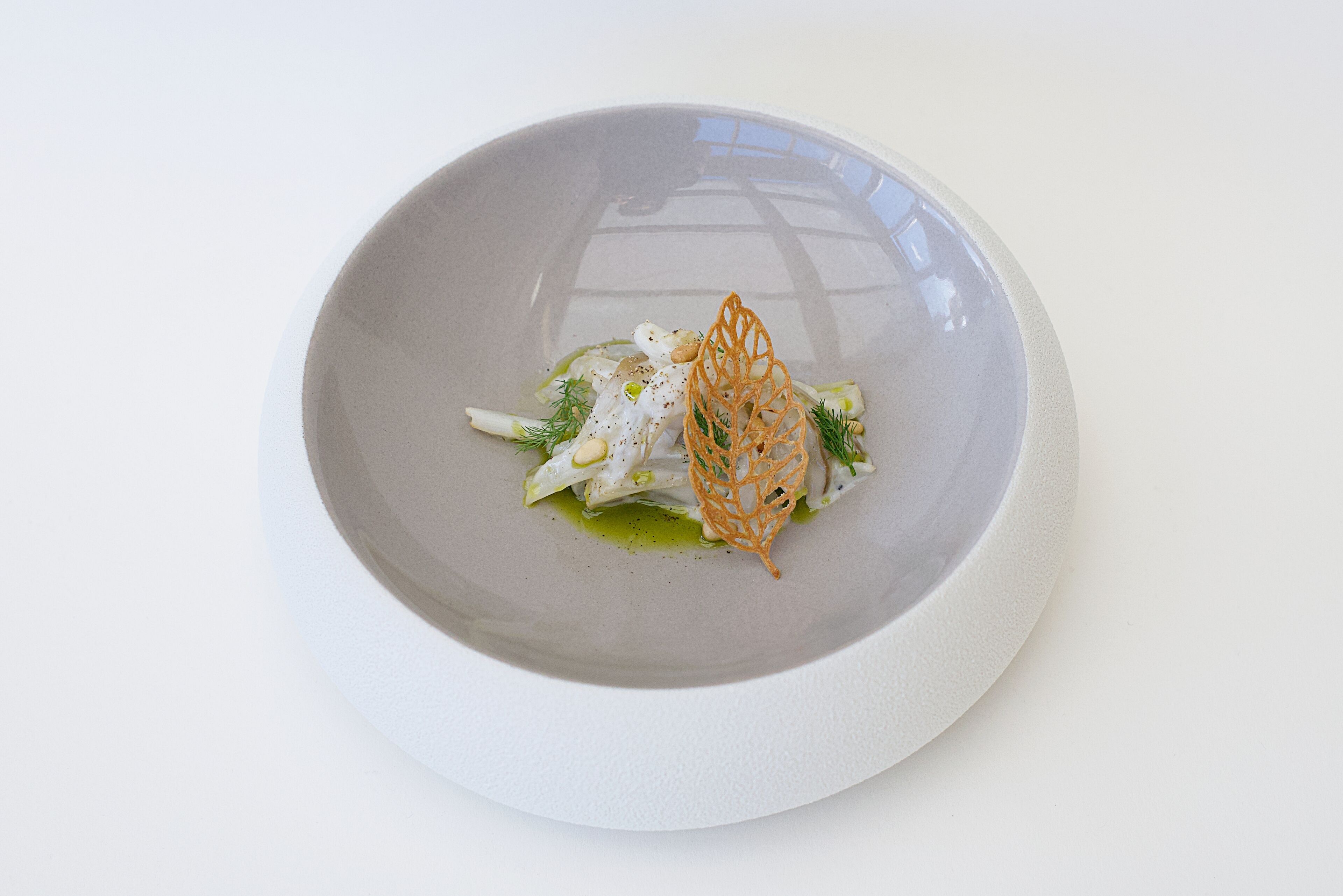 A white plate with a dish of food, including greens and a decorative element.