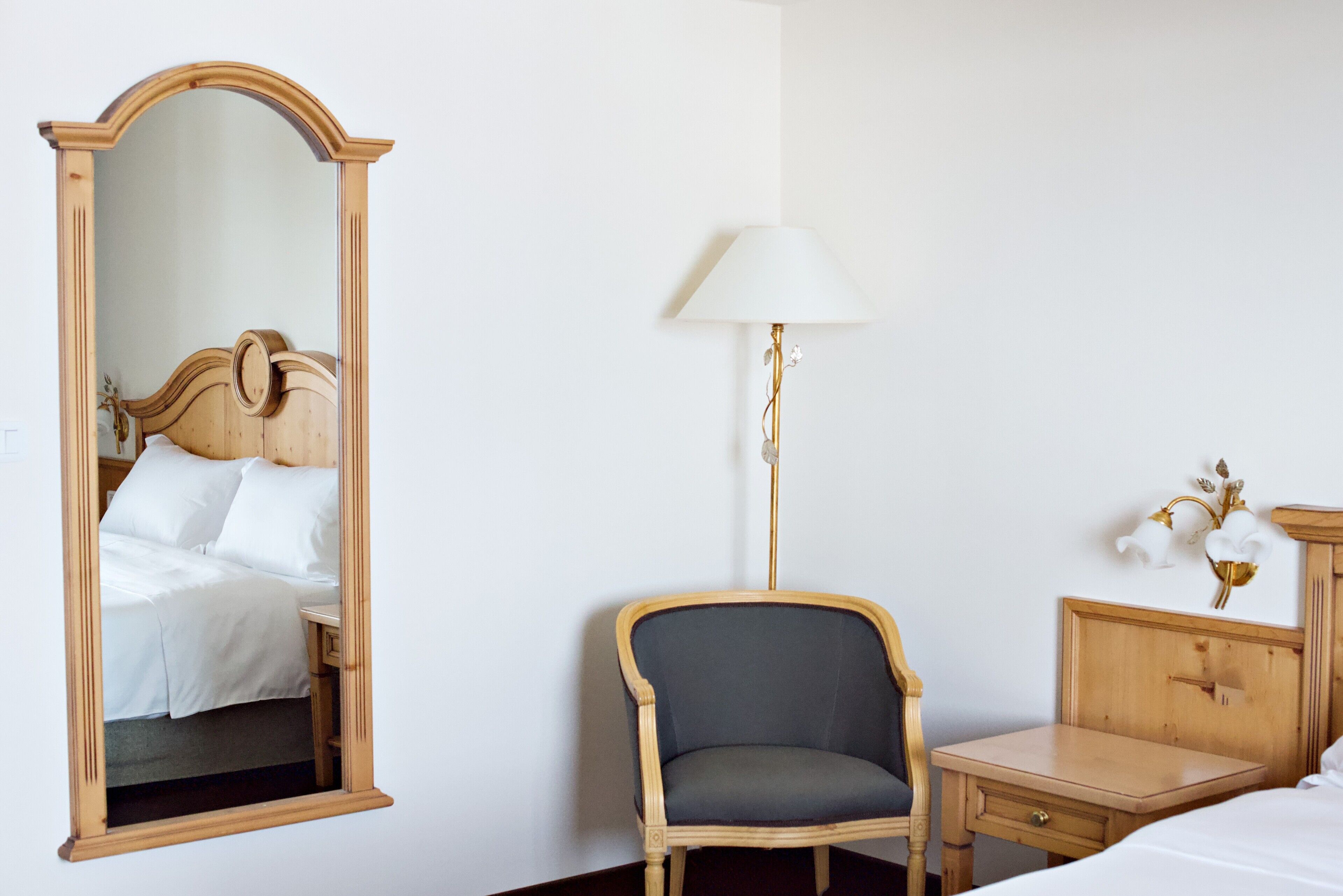 Un dormitorio con una cama de madera, un espejo, una silla, una mesita de noche y una lámpara.