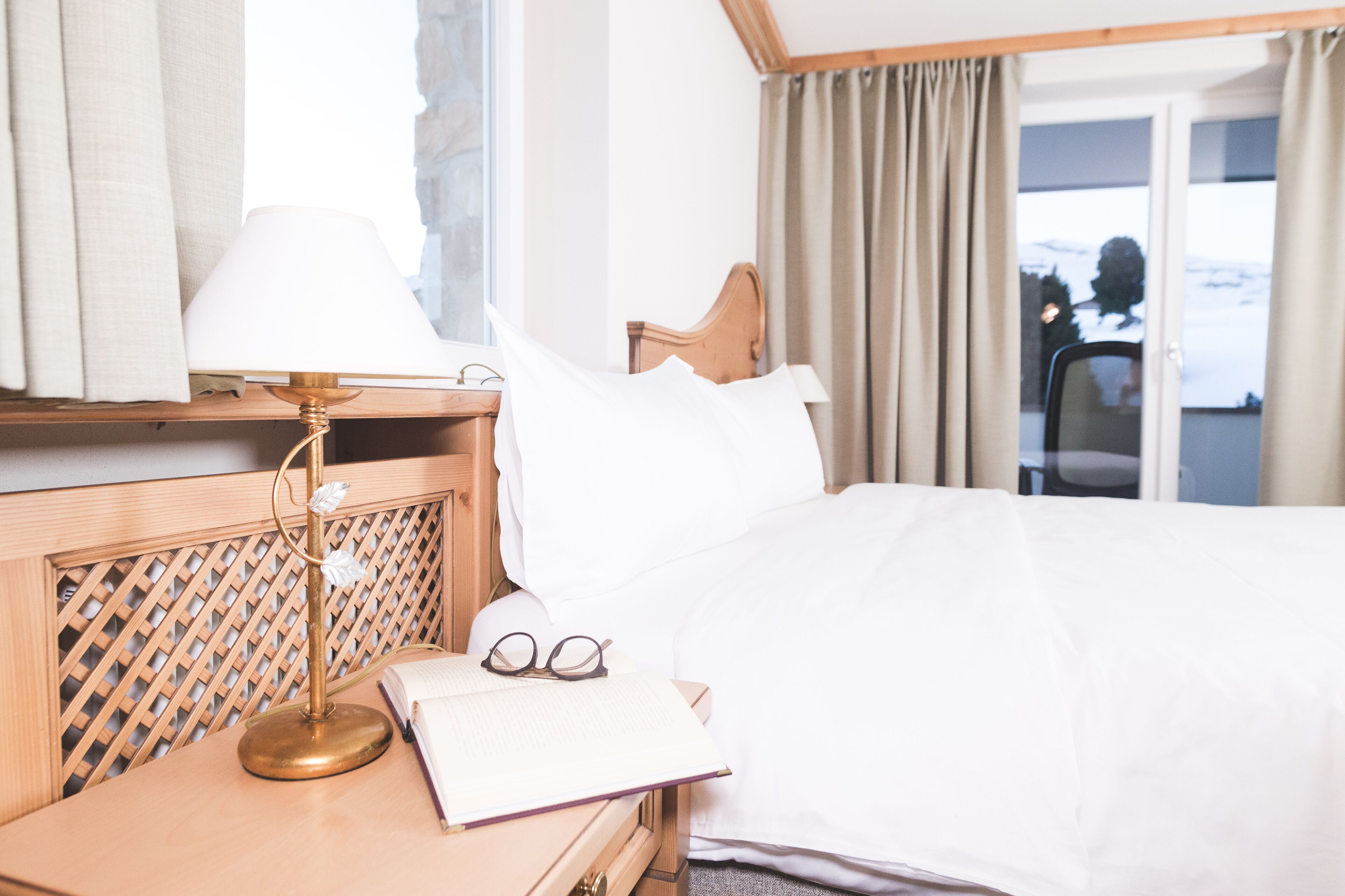 Une chambre d’hôtel avec un lit, une table de chevet avec une lampe, une paire de lunettes et un livre.