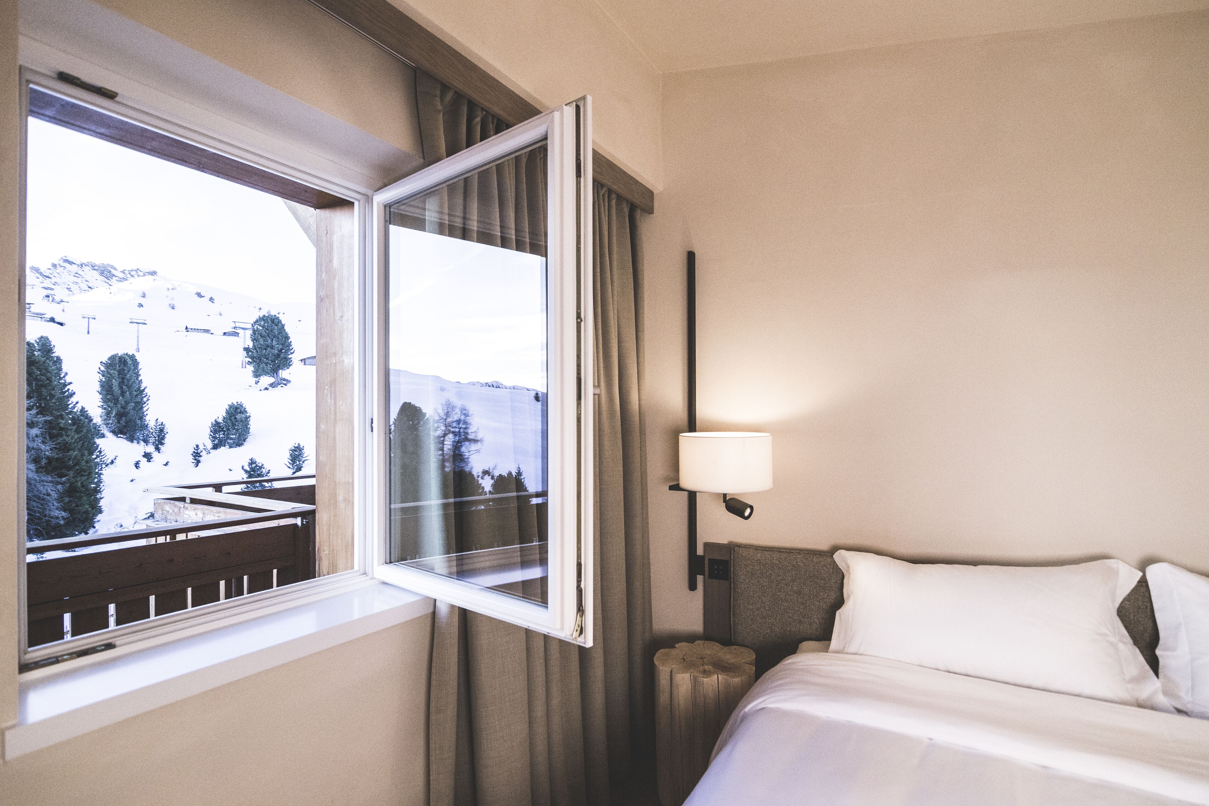 A hotel room with a bed, a nightstand, a lamp, and a window with a view of a snowy landscape.