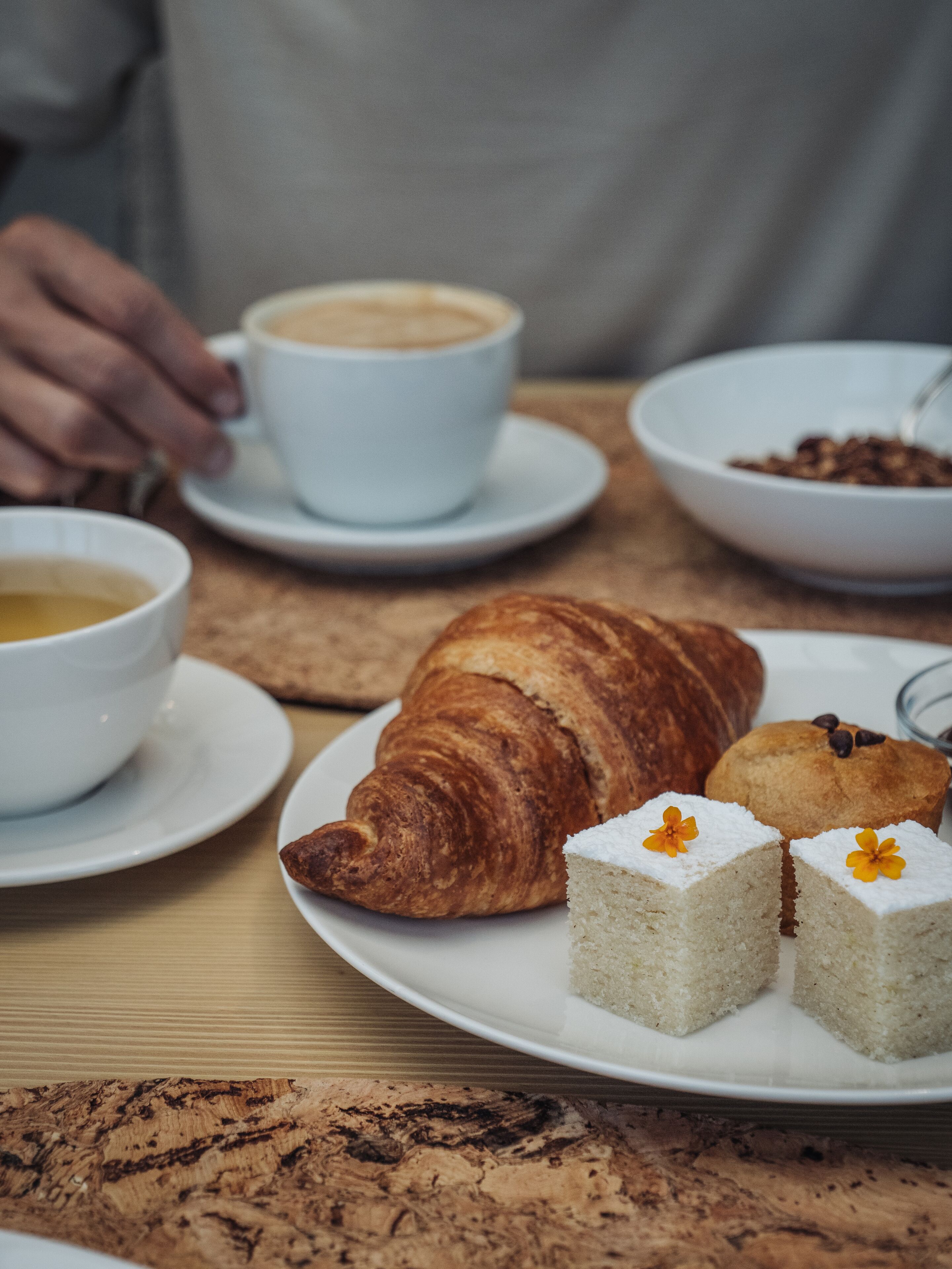 A plate with a croissant, two small cakes, and a cup of coffee on a wooden table.