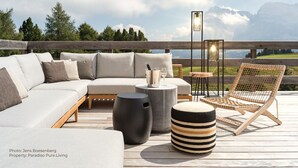 A deck with a sofa, ottoman, and chair, a table, and a lantern. - Paradiso Pure.Living Vegan Hotel (Castelrotto)