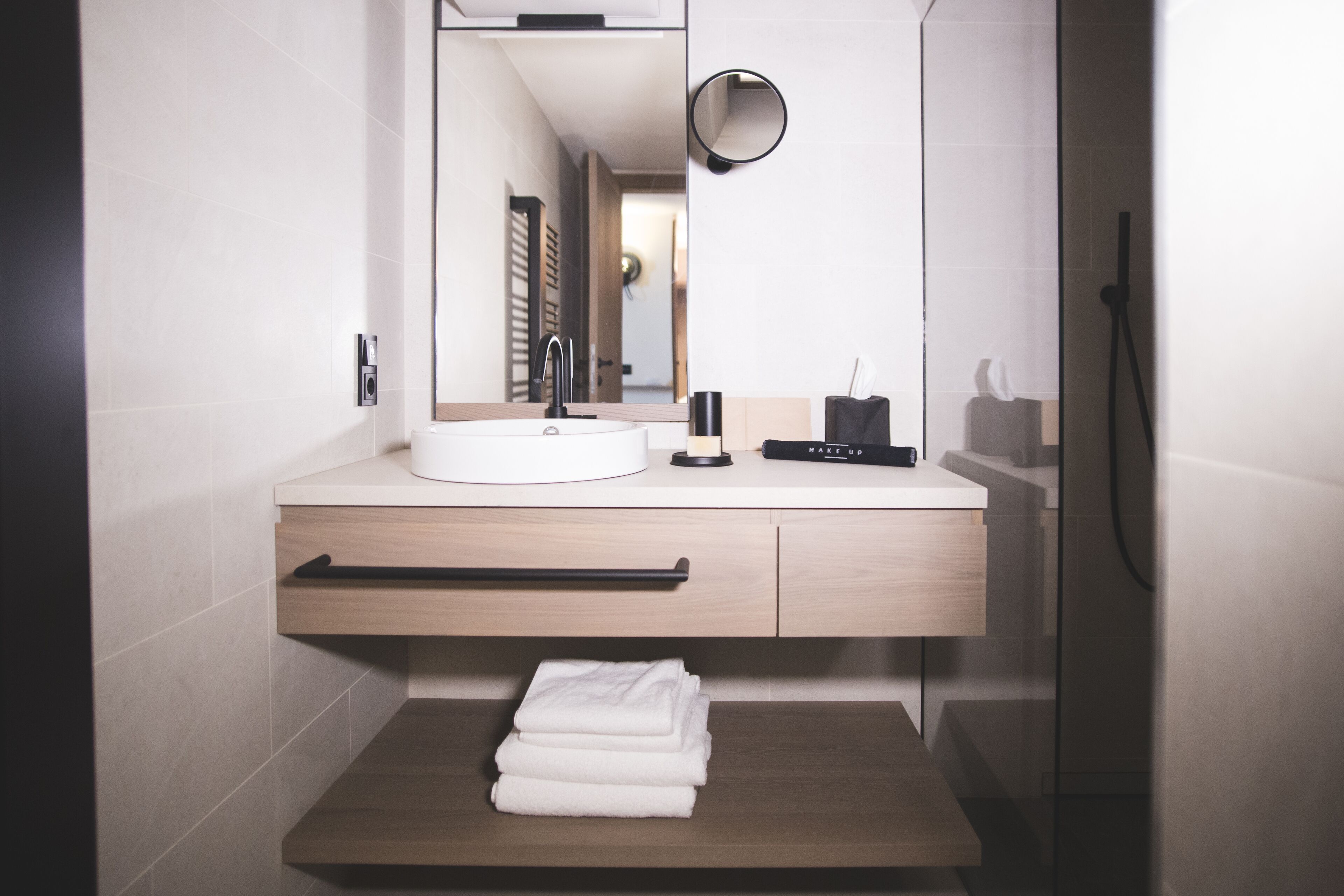 A modern bathroom with a white sink, a mirror, a towel rack, and a small shelf.