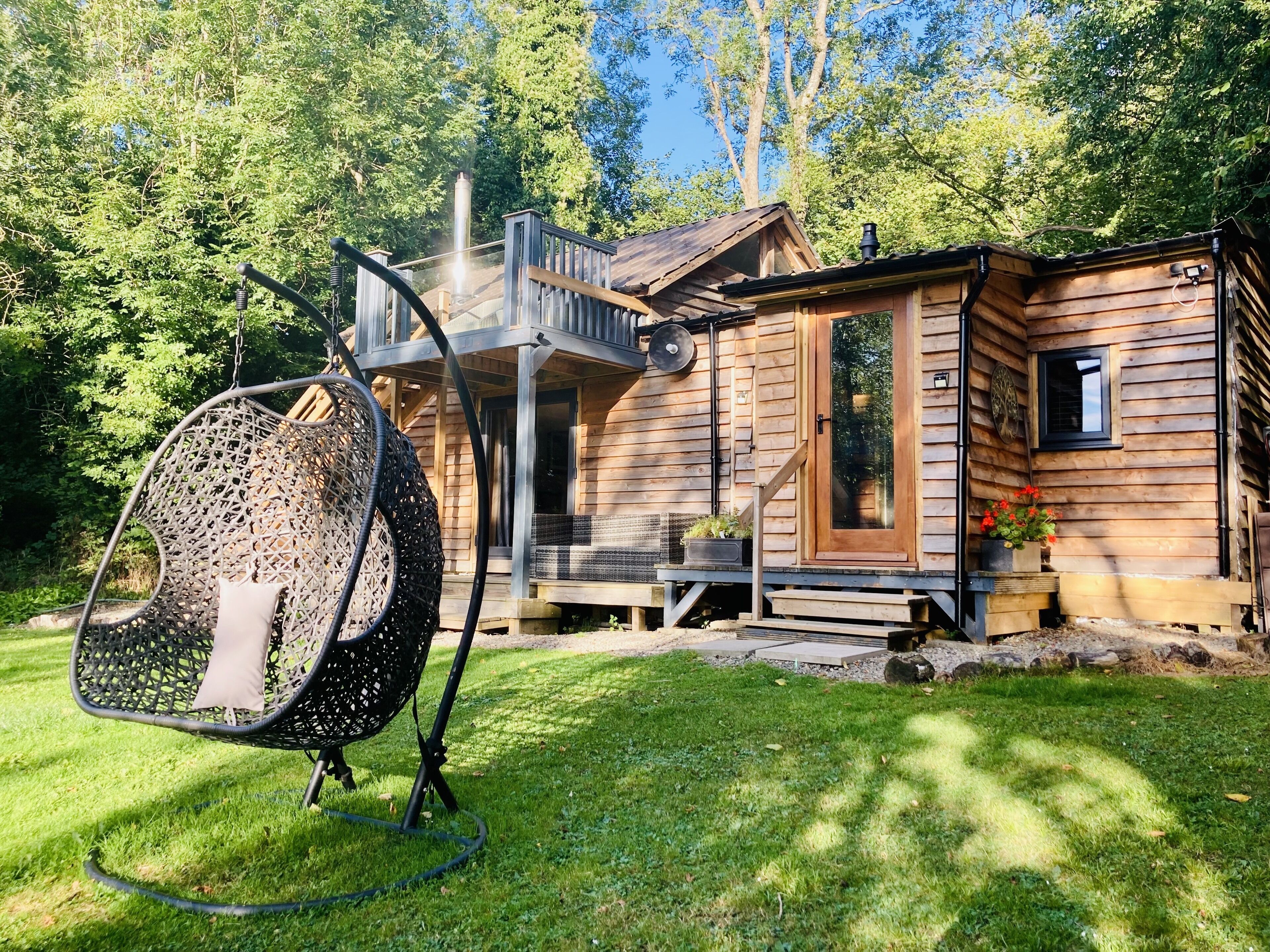 Une cabane en bois avec une véranda, un fauteuil suspendu et un petit jardin.