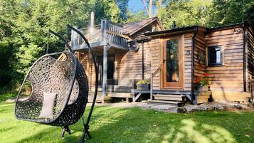 Une cabane en bois avec une véranda, un fauteuil suspendu et un petit jardin.