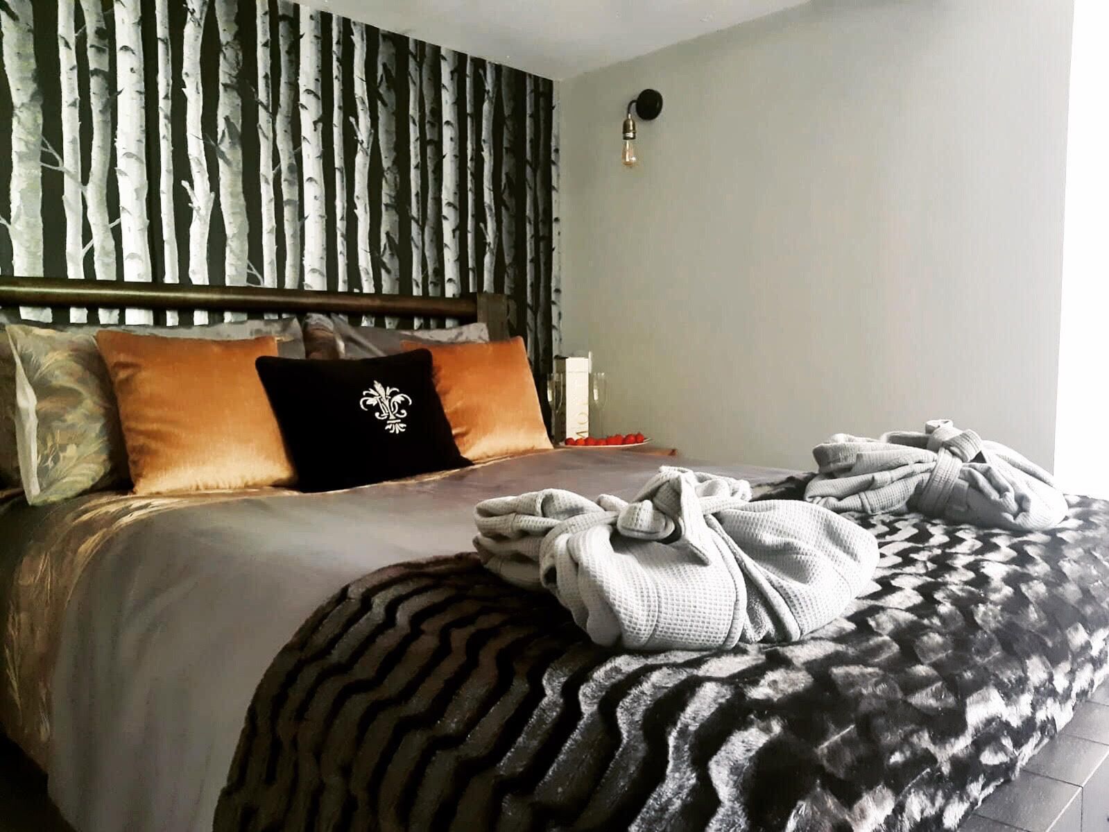 A neatly made bed with a patterned blanket, a headboard with vertical lines, and a wall-mounted light fixture.