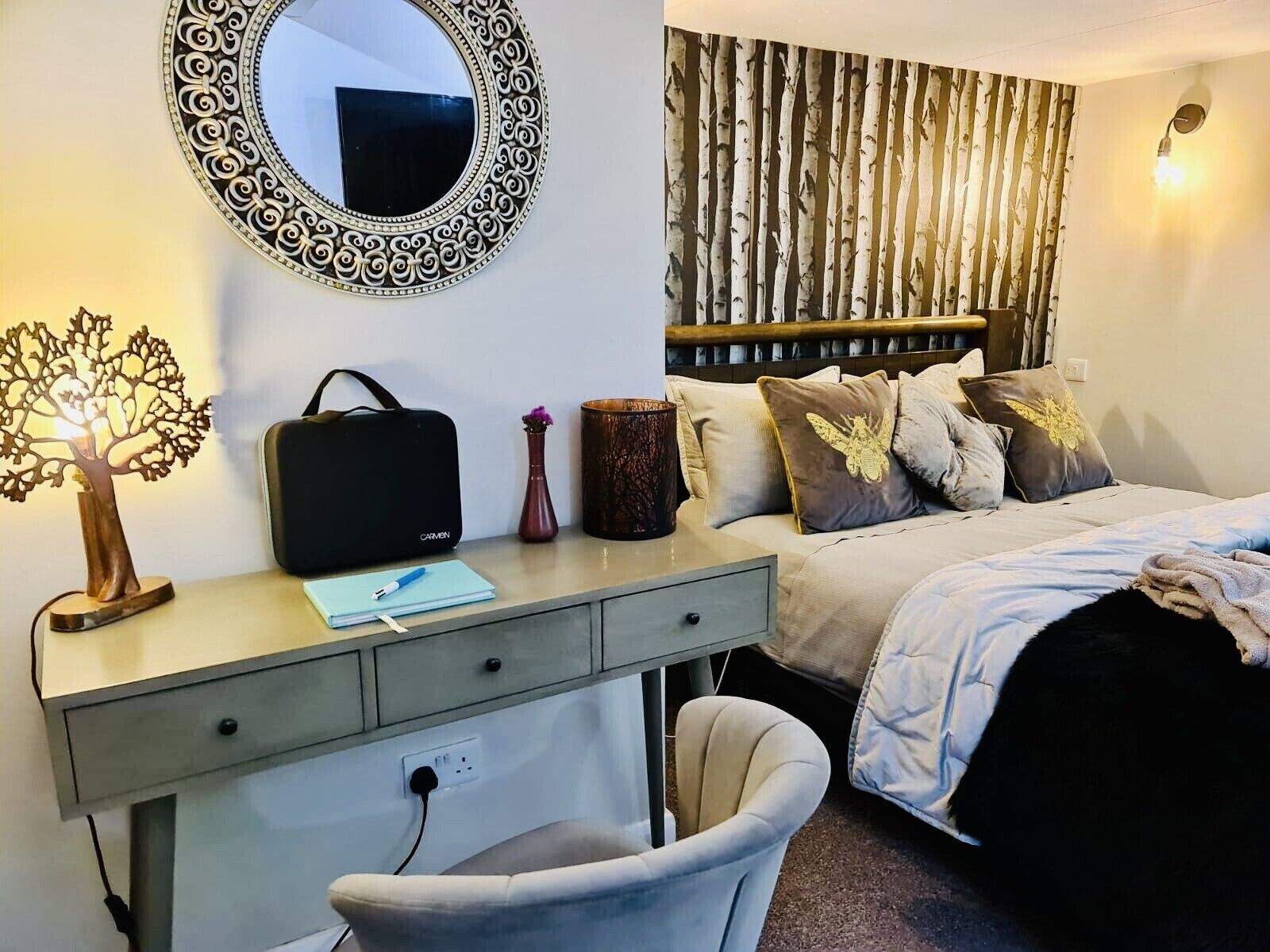 A bedroom with a bed, a desk with a chair, a mirror, and a wall with a vertical pattern.