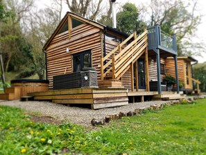 A wooden cabin with a staircase leading to a deck, surrounded by greenery.