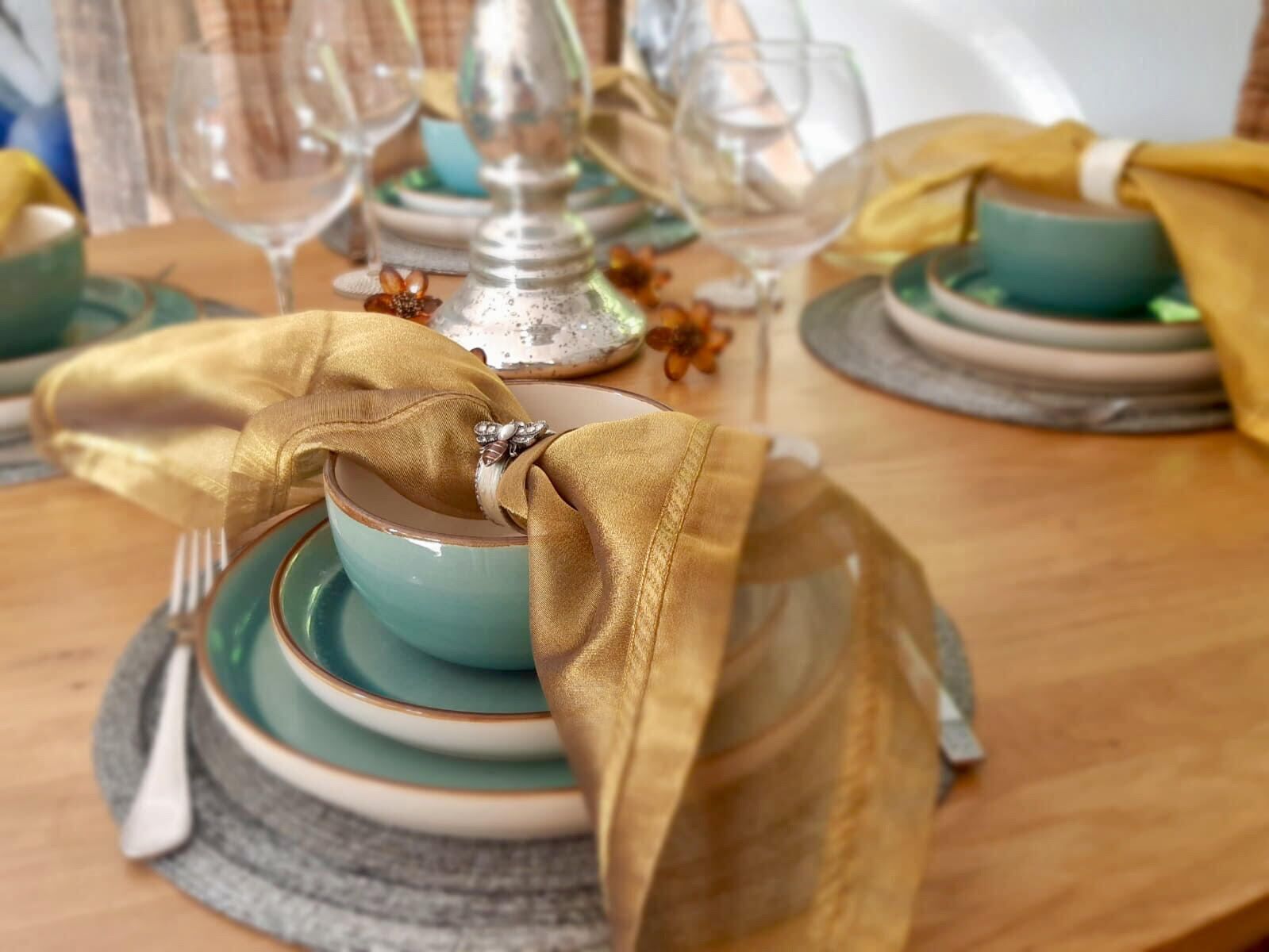 A table set with teal and gold dinnerware, a silver candelabra, and a gold napkin tied with a ribbon.