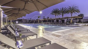 A poolside area with lounge chairs and umbrellas, a swimming pool, and palm trees.