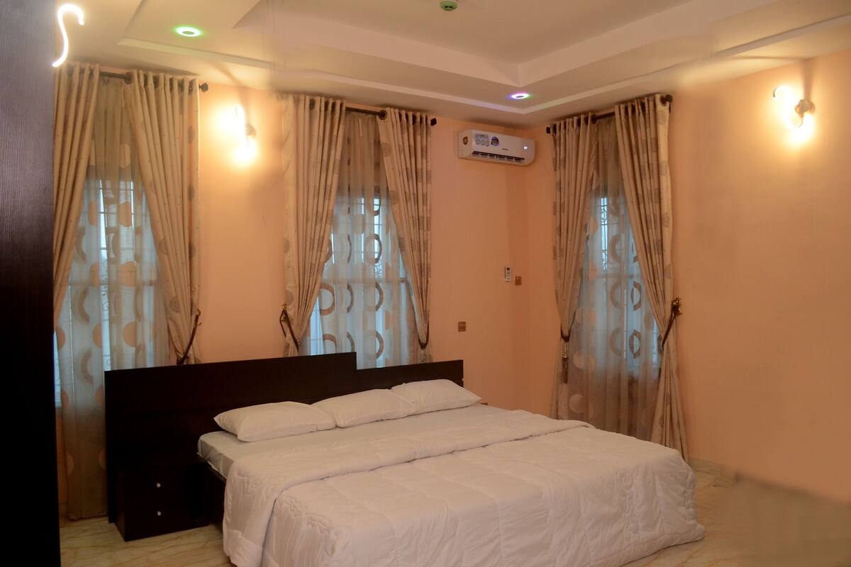Un dormitorio con cama, cortinas, un equipo de aire acondicionado y luces fijadas a la pared.