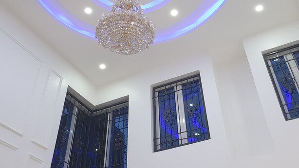 Une pièce dotée d’un plafond au design moderne, agrémenté d’un éclairage circulaire et d’un lustre.