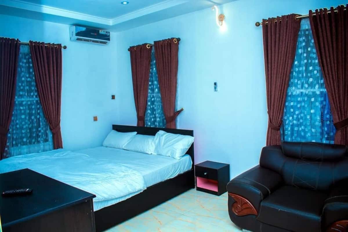 Un dormitorio con cama, mesita de noche, sillón de masaje y cortinas.