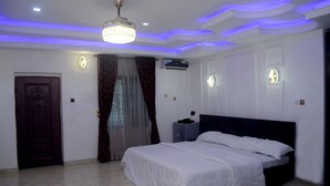 Une chambre à coucher comprenant un lit, une porte, des rideaux, un appareil de climatisation et un luminaire au plafond.