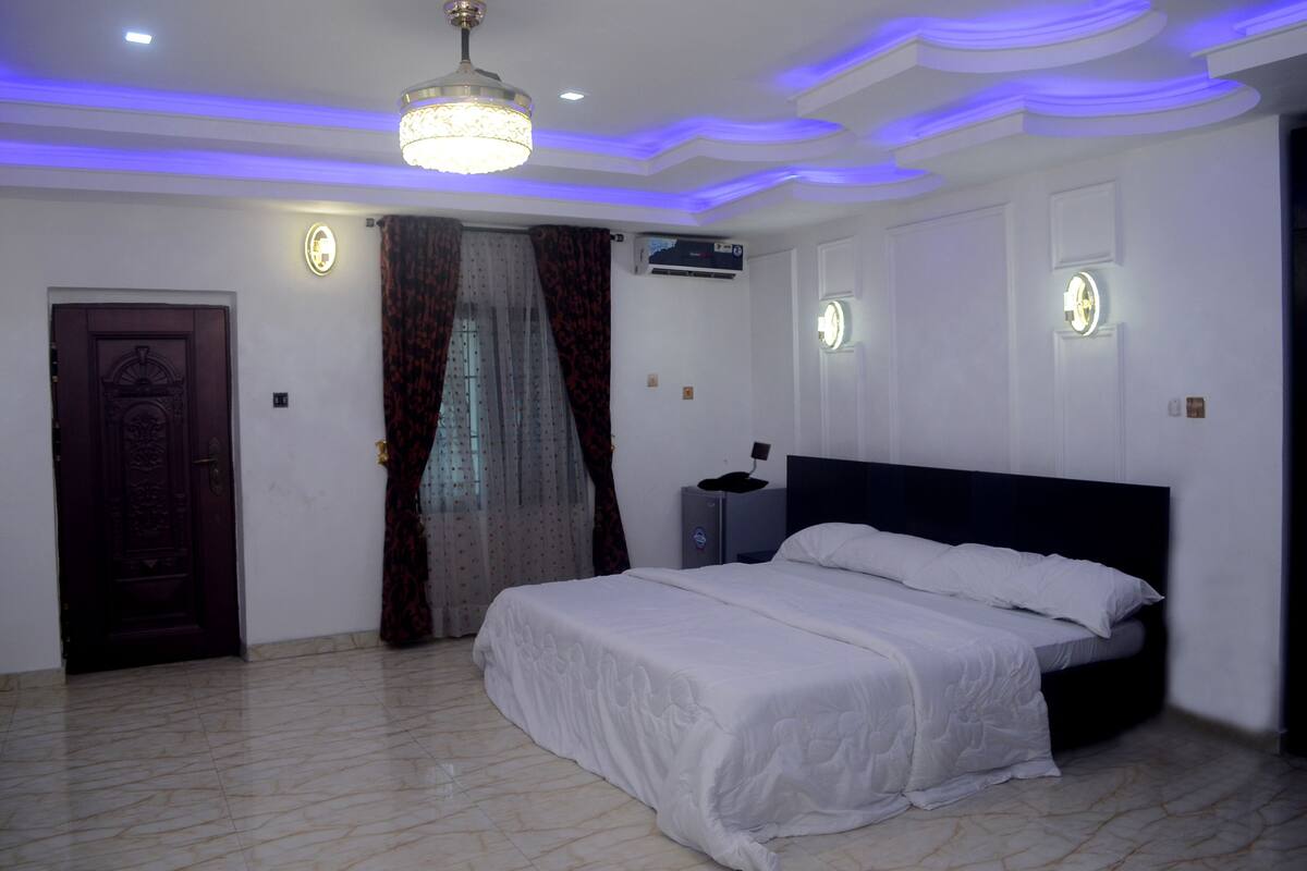 Un dormitorio con cama, una puerta, cortinas, un equipo de aire acondicionado y un accesorio de iluminación en el techo.
