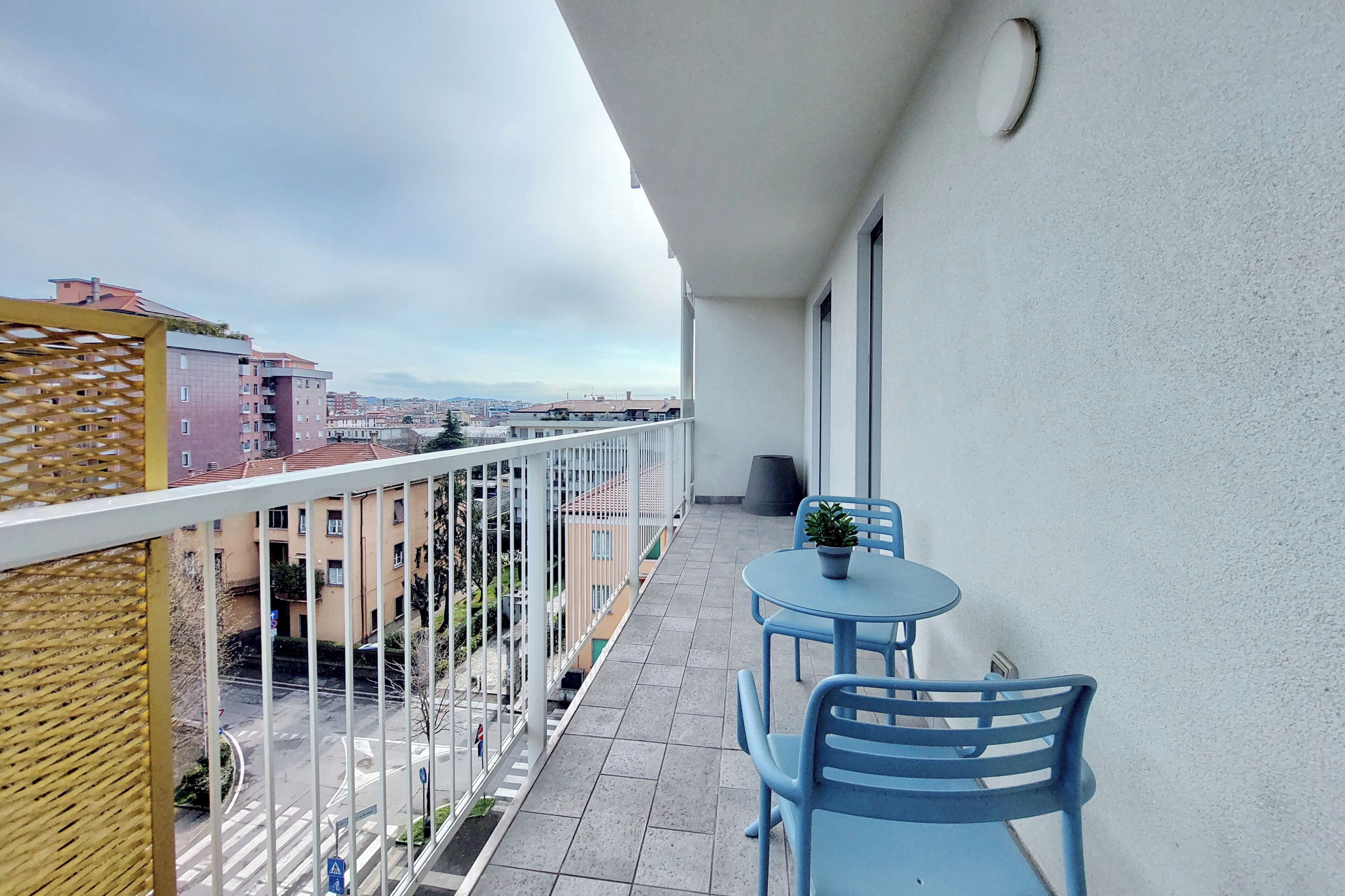 Un balcón con vistas a la ciudad, una pequeña mesa con sillas y una planta en maceta.