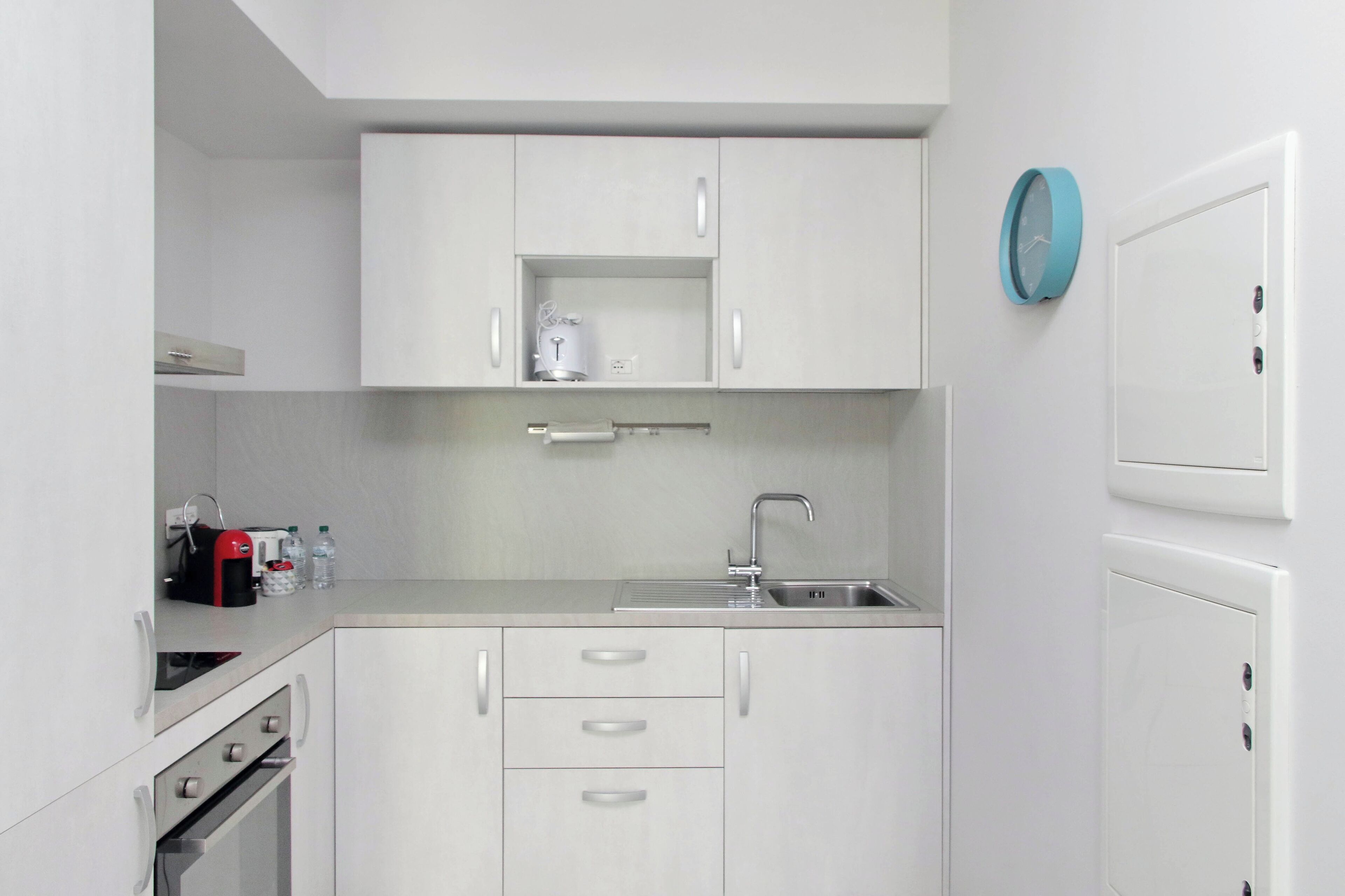 A modern kitchen with white cabinets, a stainless steel sink, and a blue clock on the wall.