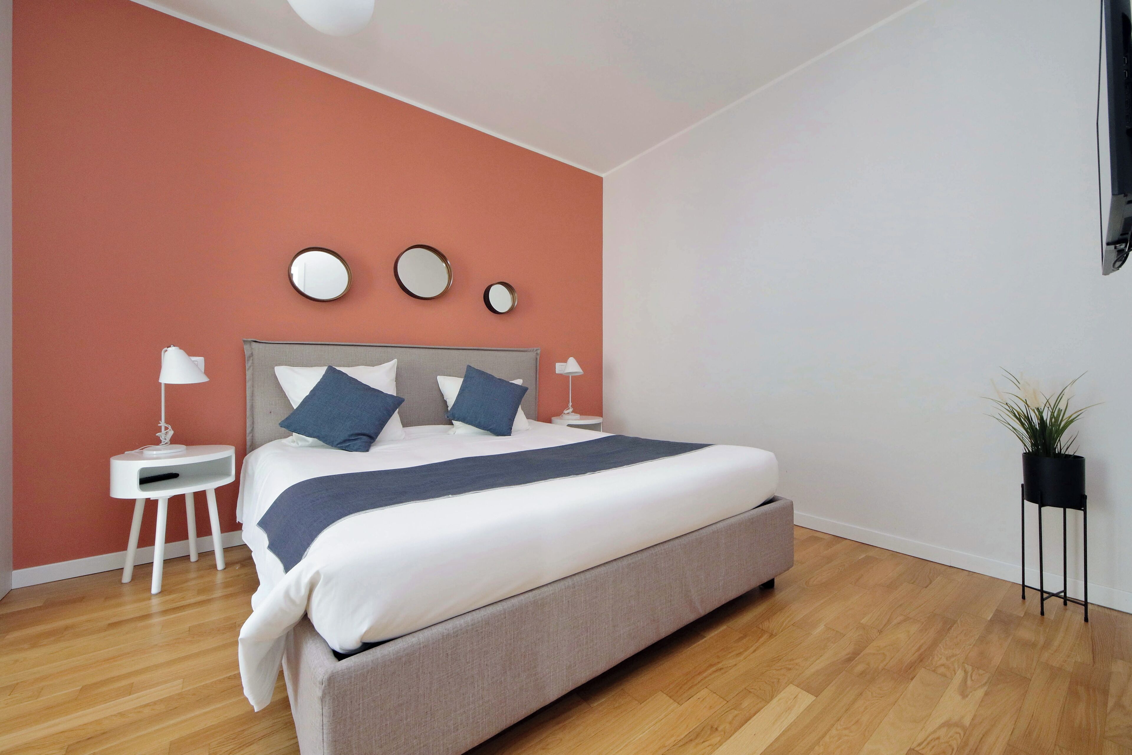 Quarto moderno com cama grande, duas mesinhas de cabeceira e espelho fixado na parede.